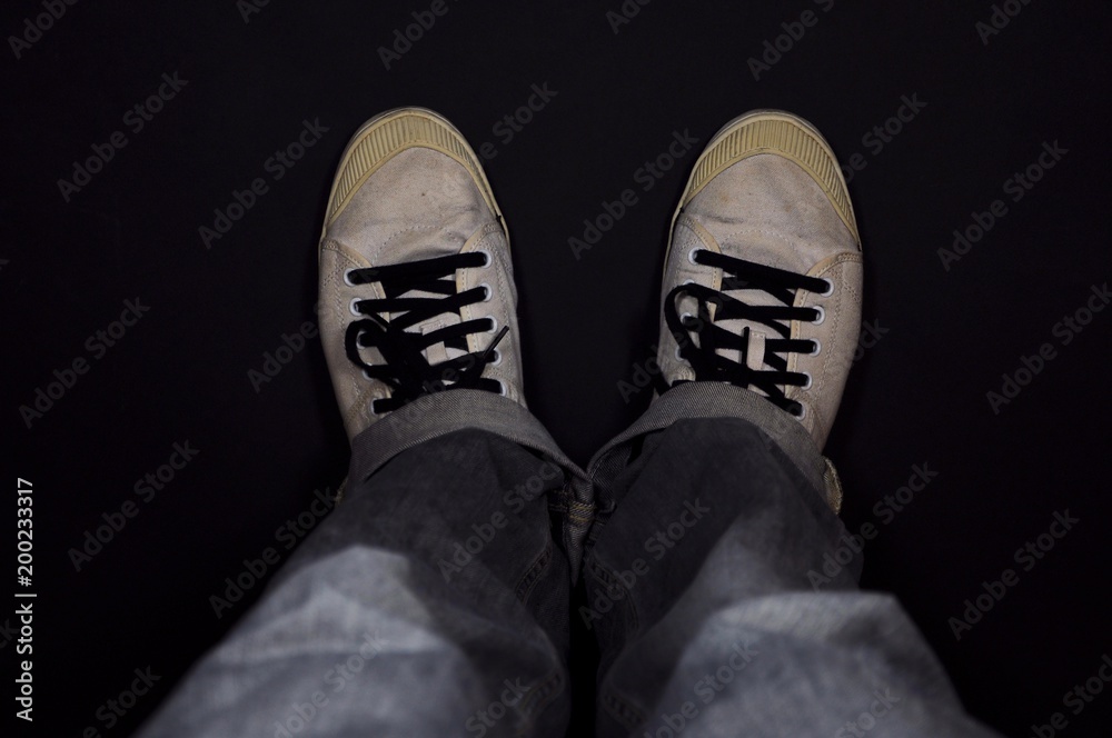 Man wearing sneakers and blue jeans on black background.