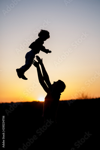 Silhouette of a man and his son playing together outdoor at sunset. Vertical photo. Family concept