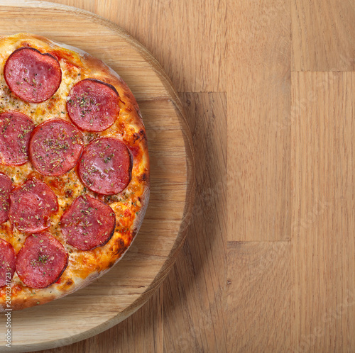 Fresh backed pizza with salami on a wooden board.