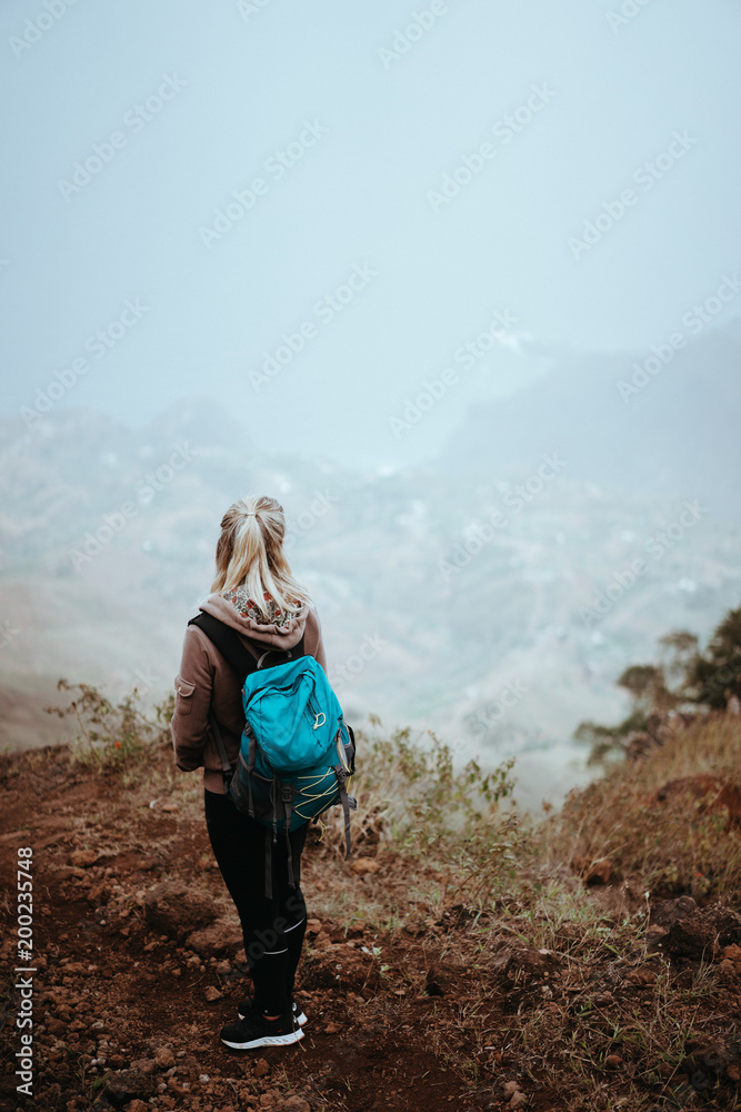 Fototapeta premium Female hiker looking down over a vertiginous misty ridge on the route to Coculi. Santo Antao Cape Verde