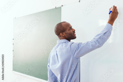 Smiling african american teacher writing on white board in classroom