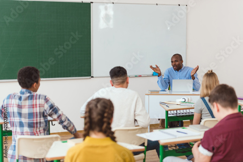 Rear view of multiethnic high school teenage students and african american teacher with wide arms