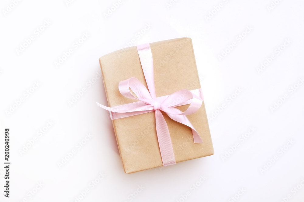 Single present wrapped in hand made craft paper gift wrap, tied w/ pastel satin bow. Giftbox, brown wrapping, giftwrap, yellow ribbon. Holiday concept. Close up, white background, copy space, top view Single present wrapped in hand made craft paper gift wrap, tied w/ pastel satin bow. Giftbox, brown wrapping, giftwrap, yellow ribbon. Holiday concept. Close up, white background, copy space, top view