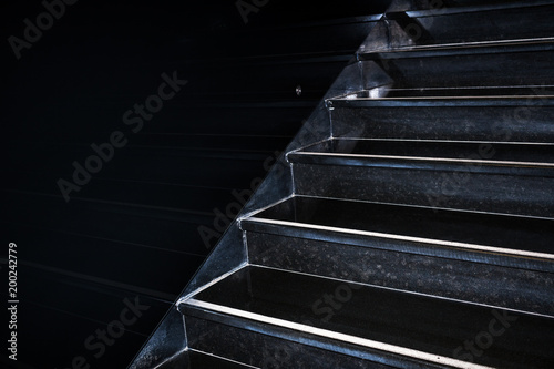 Black granite staircase going diagonally upward reflecting in black wall with copy space.
