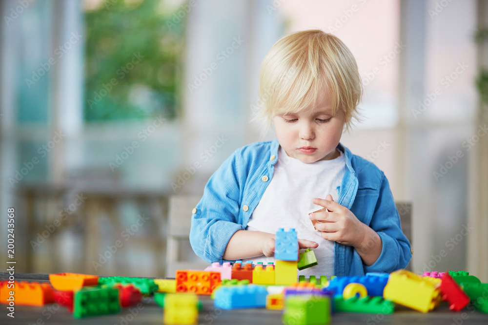 Little boy playing with colorful plastic construction blocks