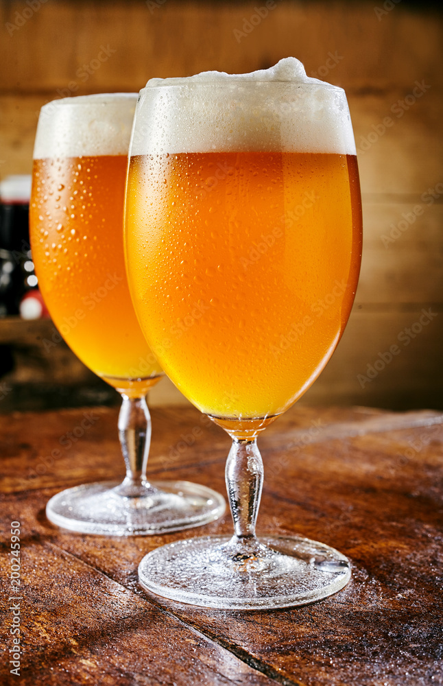 Two glasses of cold beer standing on wooden table Two glasses of cold beer standing on wooden table