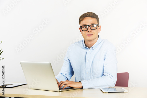 Happy young businessman using laptop at his office desk, smiling and wear glasses.