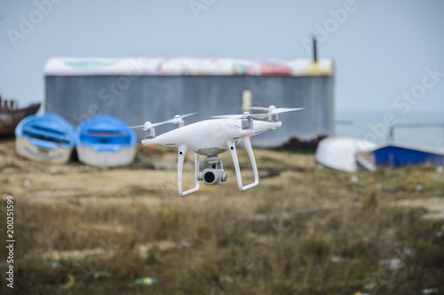 Drone flying in front of a blurry background of boats and depot.