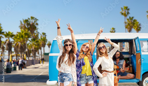 summer holidays, road trip, travel and vacation concept - happy young hippie friends having fun and dancing over minivan car and venice beach in los angeles background