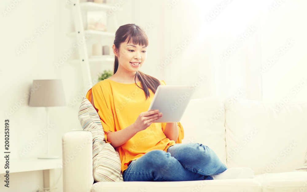 people, technology and leisure concept - happy young asian woman sitting on sofa with tablet pc computer at home people, technology and leisure concept - happy young asian woman sitting on sofa with tablet pc computer at home