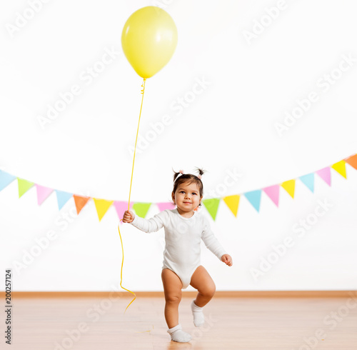 childhood, people and celebration concept - happy baby girl with helium balloons on birthday party