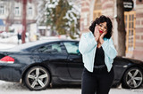 Stylish african american plus size model with mobile phone at hand  at winter snowy day against black car.