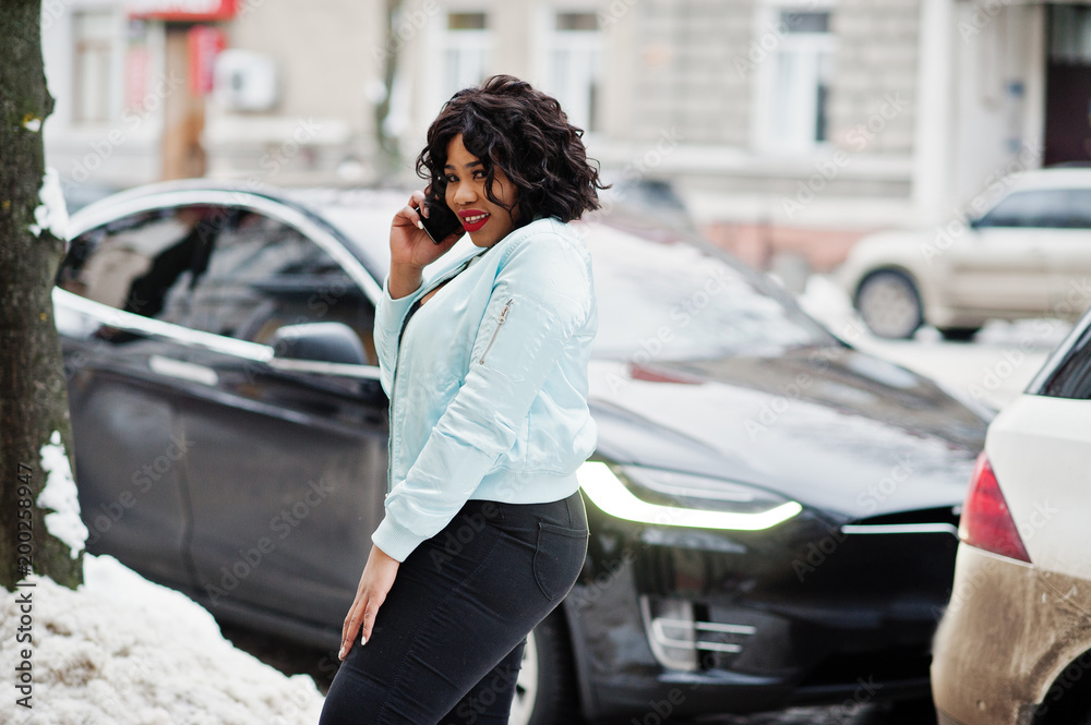 Stylish african american plus size model with mobile phone against electro car. Stylish african american plus size model with mobile phone against electro car.