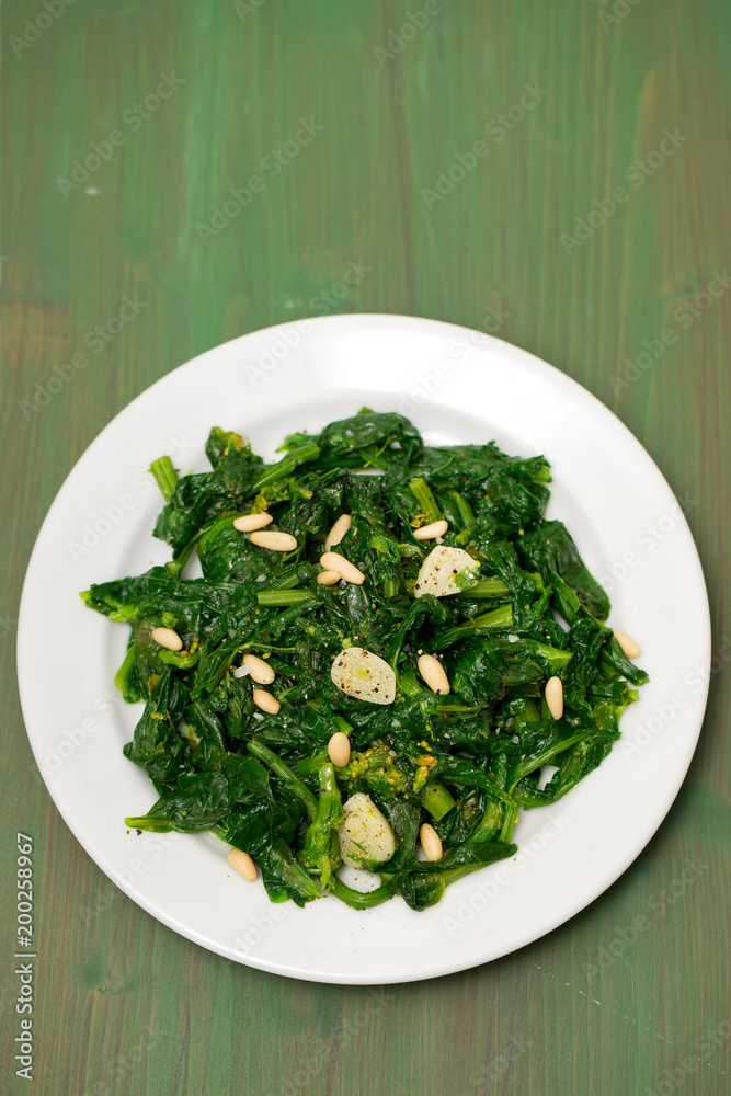 greens with garlic on white plate on wooden background