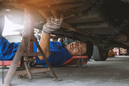 Auto mechanic working under a car, .mechanic lying and repairing under car at the repair garage, Mechanic in blue uniform lying down and working under car at the repair garage photo