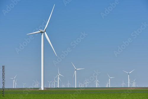 Eolian farm renewable energy in fresh green field against clear blue sky