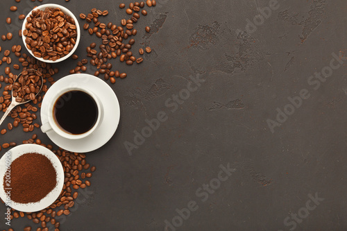 Cup of black coffee and scattered beans on gray background