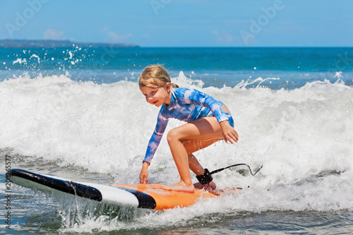 Photography Happy baby girl - young surfer ride on surfboard with fun on sea waves