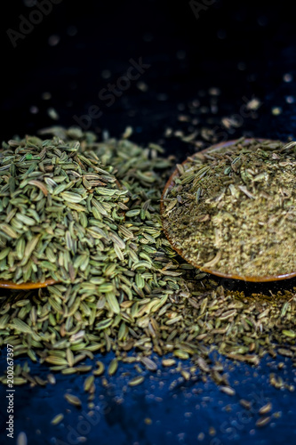 Close up of raw dried fennel seeds or variyali or Foeniculum vulgare on a wooden surface with its powder. photo
