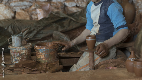 pottery, workshop, ceramics art concept - closeup on young ceramist hands with unbaked clay jug, craftsman stand at a workplace, hands holds the clay cup and tools