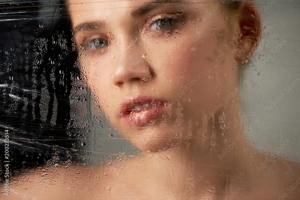 Portrait of young beautiful girl in Studio, with professional makeup. Beauty shooting. In the face of a transparent glass with water droplets. Hydration of the skin