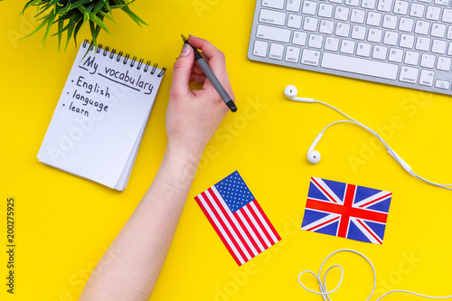 Learn new english vocabulary. Learn landuage concept. Computer keyboard, british and american flags, notebook for writing new vocabulary on yellow background top view photo