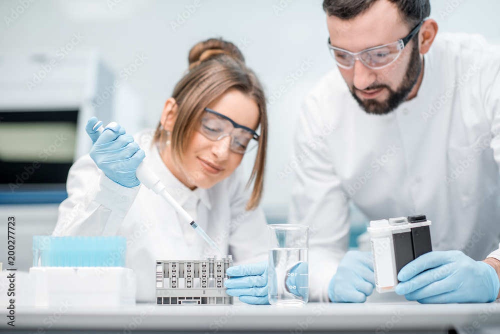 Laboratory assistants in uniform and protective glasses working with test tubes in the medical laboratory Laboratory assistants in uniform and protective glasses working with test tubes in the medical laboratory