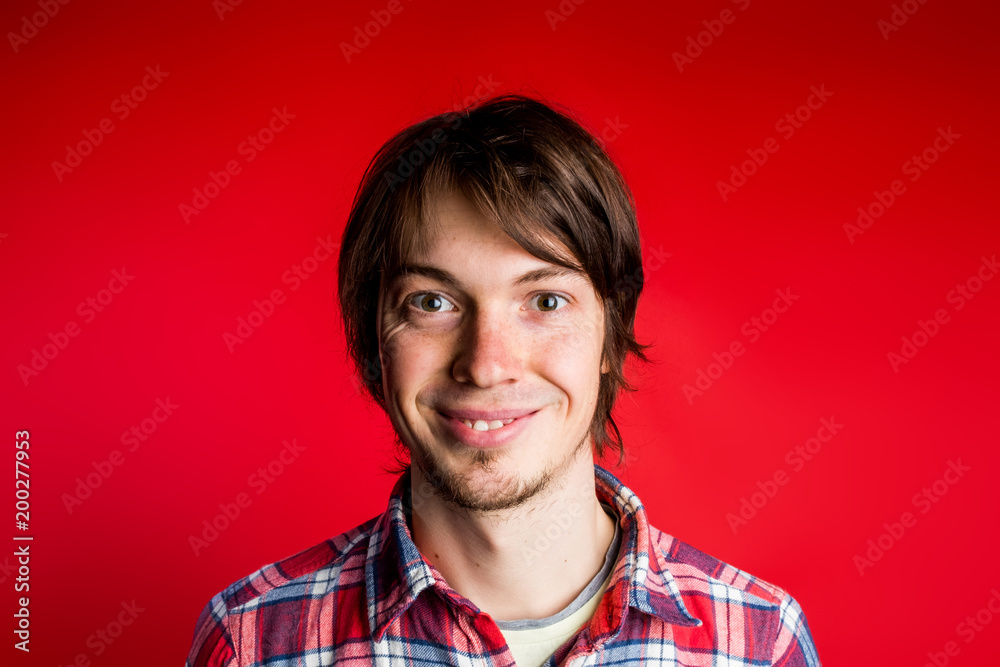 Hipster smiles and looks at camera close-up portrait, in plaid shirt on red background. Hipster smiles and looks at camera close-up portrait, in plaid shirt on red background.