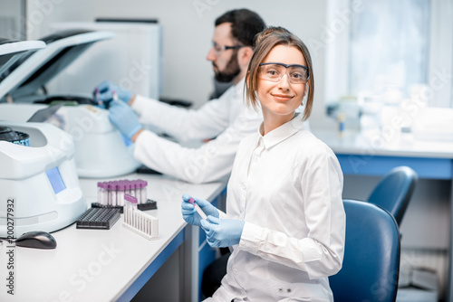 Portrait of a young female laboratory assistant making analysis with test tubes and analyzer machines sitting at the modern laboratory