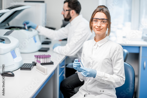 Portrait of a young female laboratory assistant making analysis with test tubes and analyzer machines sitting at the modern laboratory