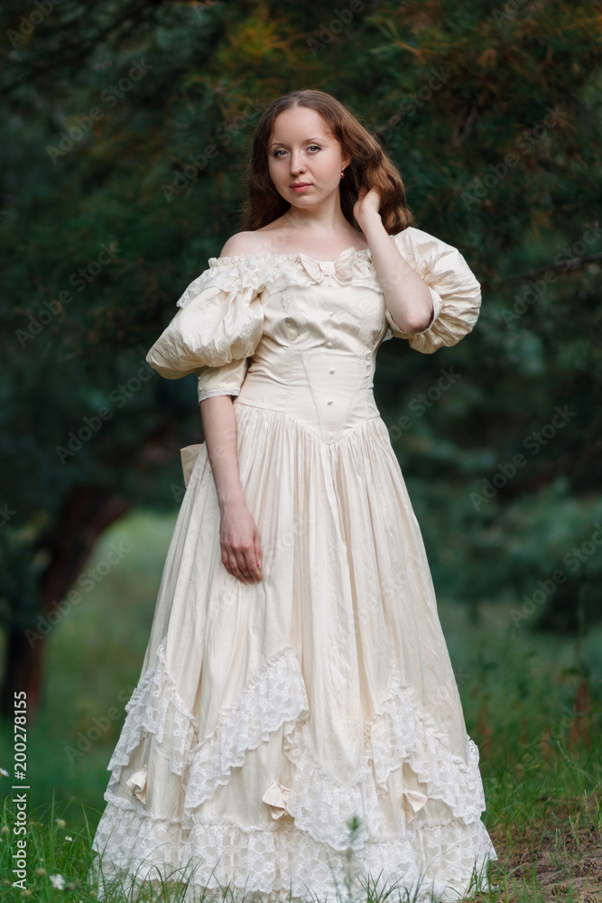 Beautiful brunette in a vintage dress. A nice young girl in a classic outfit. A woman in a stylish vintage dress. Style of the queen. Classical attire of the princess. A woman is walking in the woods.