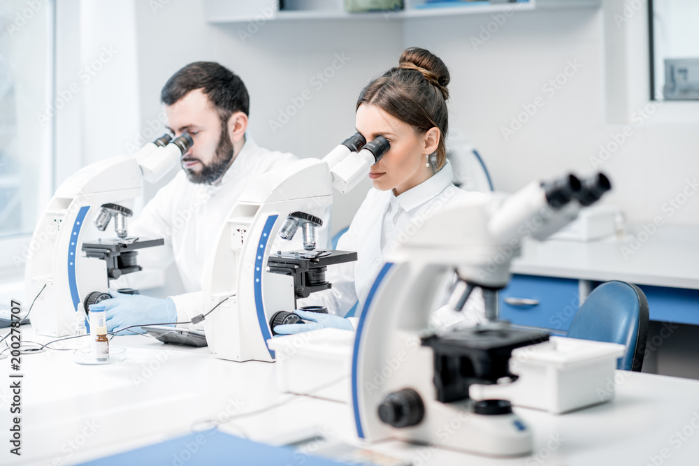 Obraz premium Couple of medics in uniform working with microscope making analysis at the laboratory office