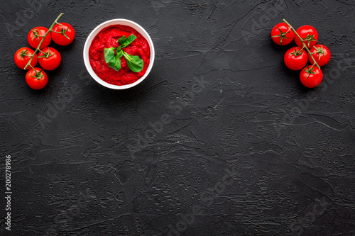 Tomato sauce in bowl with green basil near cherry tomatoes on black background top view space for text