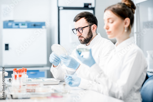 Couple of medics in uniform making bacteriological tests sitting in the modern laboratory