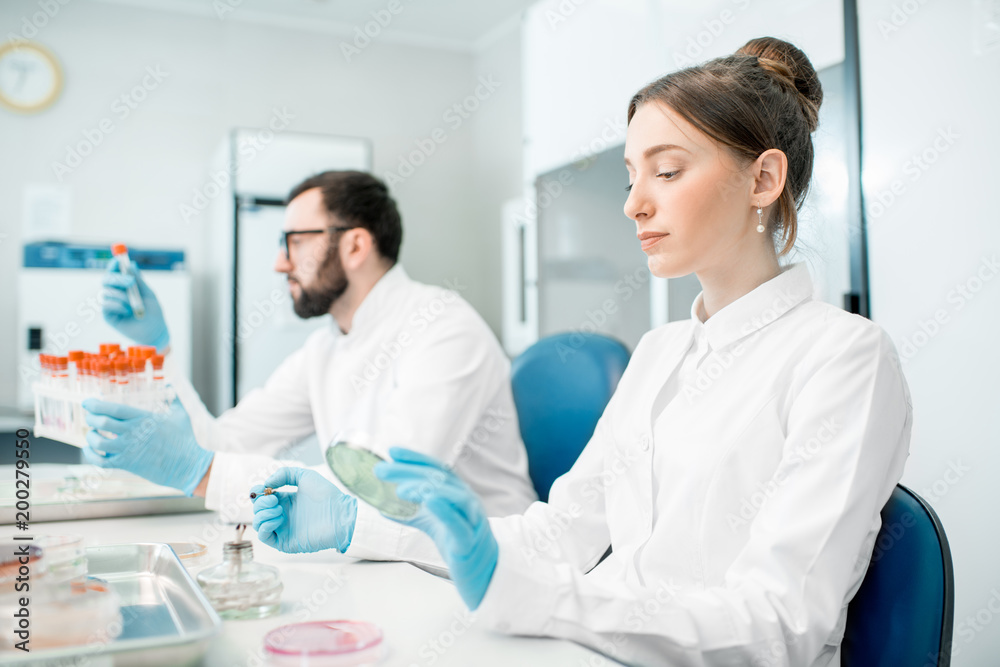 Couple of medics in uniform making bacteriological tests sitting in the modern laboratory Couple of medics in uniform making bacteriological tests sitting in the modern laboratory