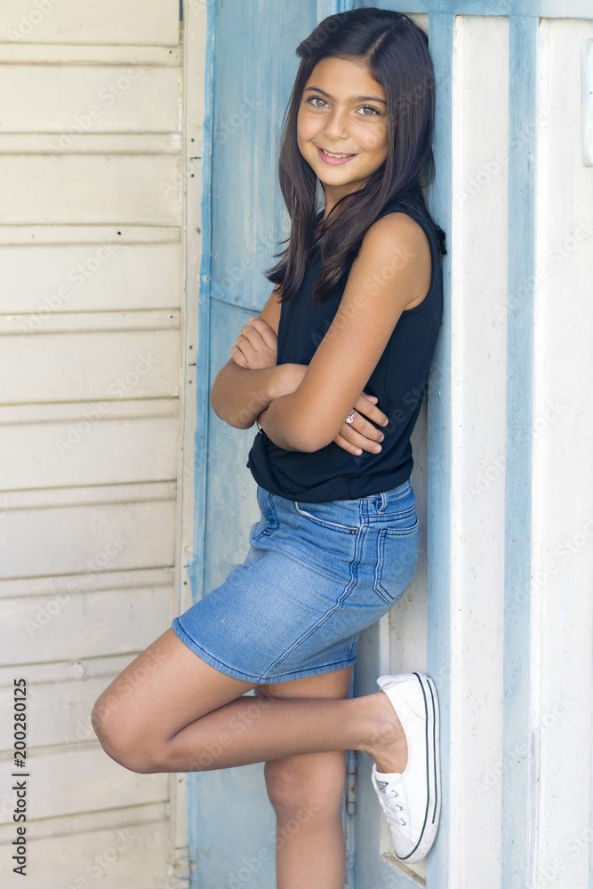 Portrait of a cute little girl in garden. Outdoor portrait of a smiling brunette girl, white wall in background. Portrait of a cute little girl in garden. Outdoor portrait of a smiling brunette girl, white wall in background.