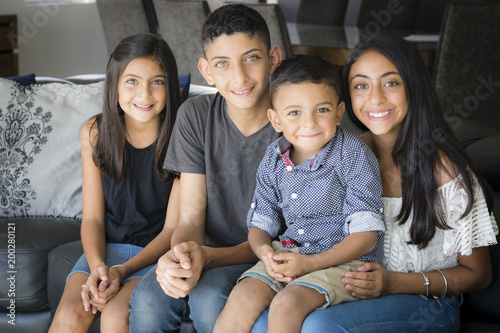 Smiling siblings in the living room. Two brothers and two sisters sitting on the couch smiling.