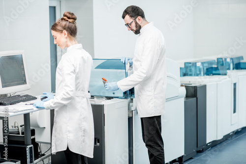 Couple of medics configuring analyzer machine in the modern laboratory