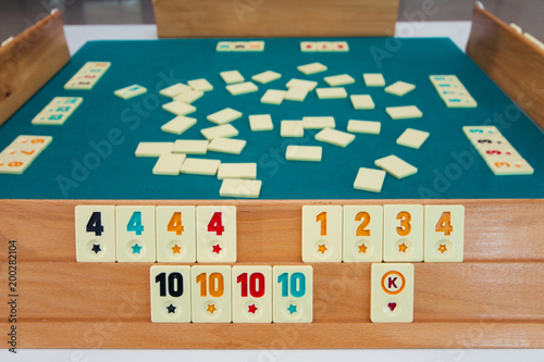 Turkish board game Okey (Rummikub). A table with green cloth and chips. Hands of the players. photo
