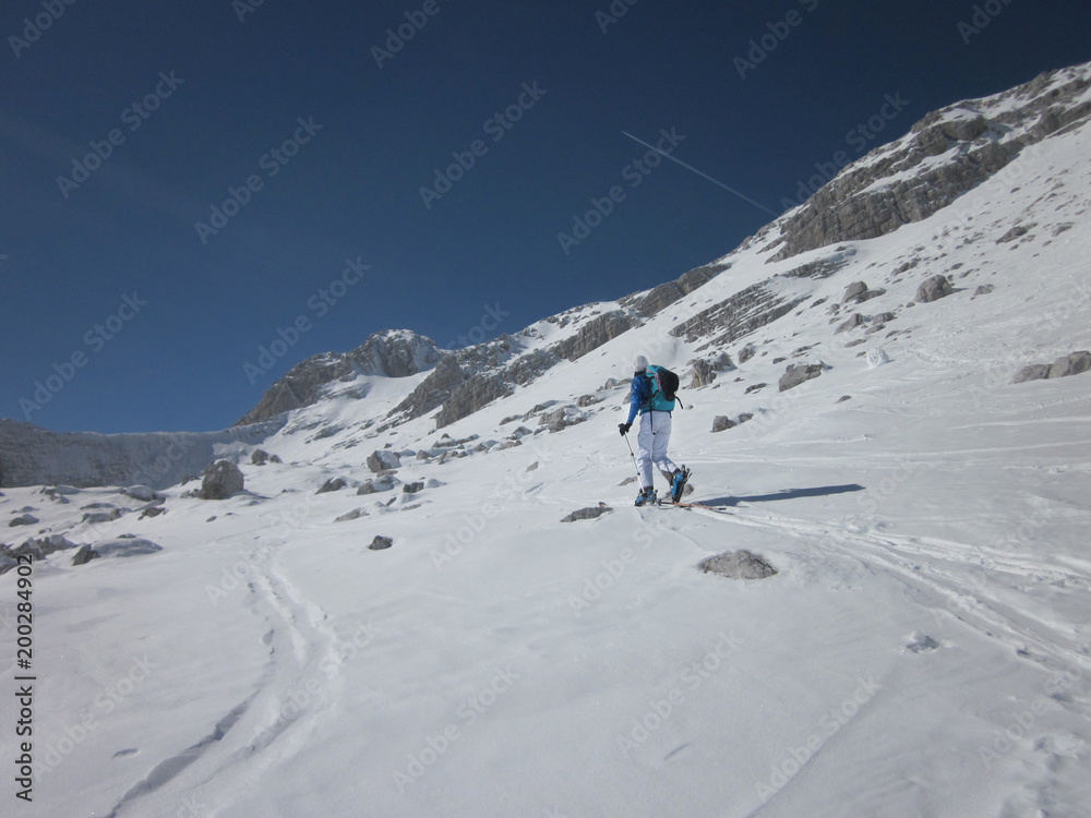 Snow covered landscape and woman climbing on touring skis