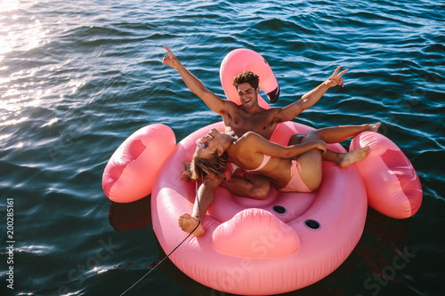 Fotografie Excited couple riding on inflatable toy behind a boat