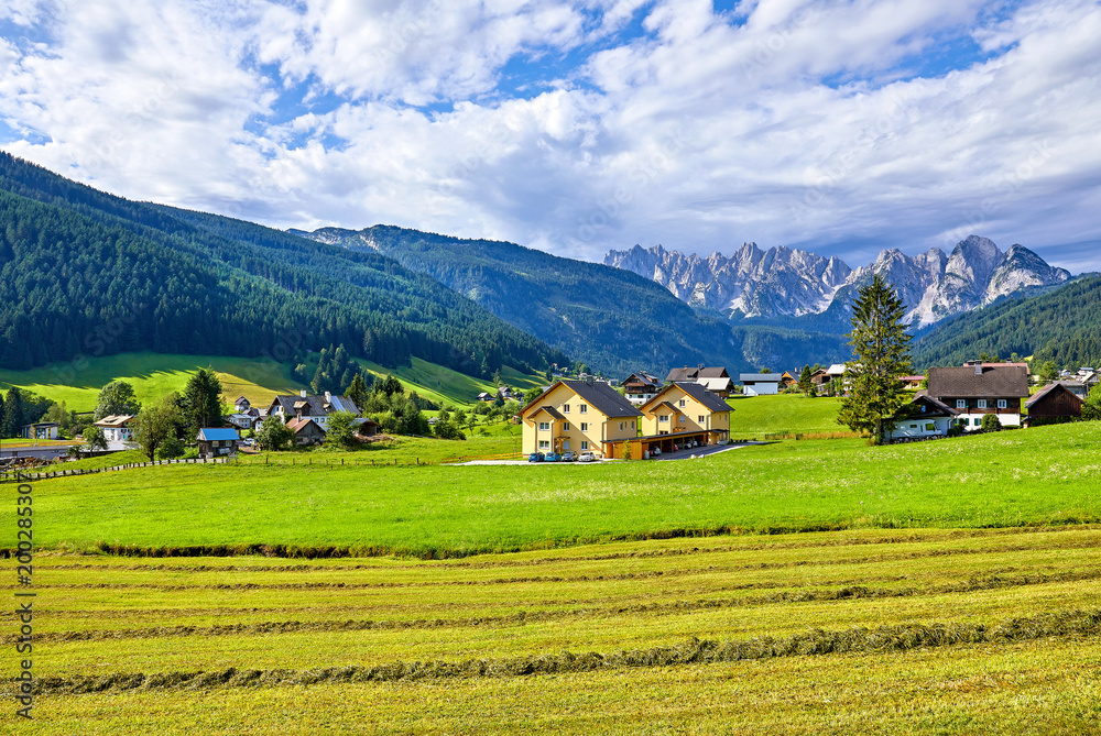 Austrian village among meadows fields and Alpine mountains.