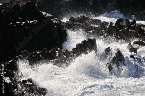 Spritzende Gischt auf schwarzen Felsen in der Sonne