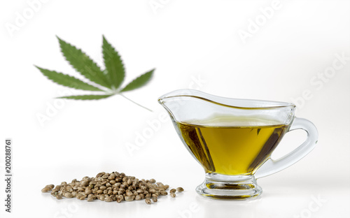 Hemp seeds, hempseed oil in a glass gravy boat and marijuana leaf isolated on a white background.