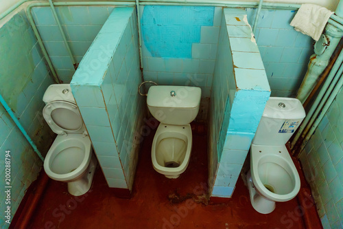 Old public toilet with three toilet bowls and red painted floor