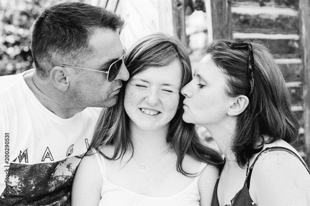 mom and dad kiss their teen daughter on black and white photography. The girl has freckles on her face mom and dad kiss their teen daughter on black and white photography. The girl has freckles on her face