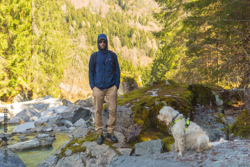 Young Italian man going for hiking in the forest with friendly white wire-haired breed dog spinone italiano along the mountain river with clean transparent water on a sunny day Trentino, Italy, Europe Young Italian man going for hiking in the forest with friendly white wire-haired breed dog spinone italiano along the mountain river with clean transparent water on a sunny day Trentino, Italy, Europe