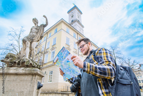 young adult tourist man with camera and backpack watch map. travel concept. copy space