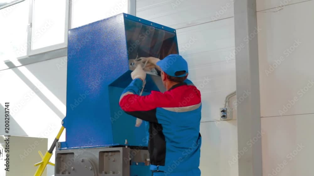 Worker loads sorted plastic in automated plastic recycling machine Worker loads sorted plastic in automated plastic recycling machine