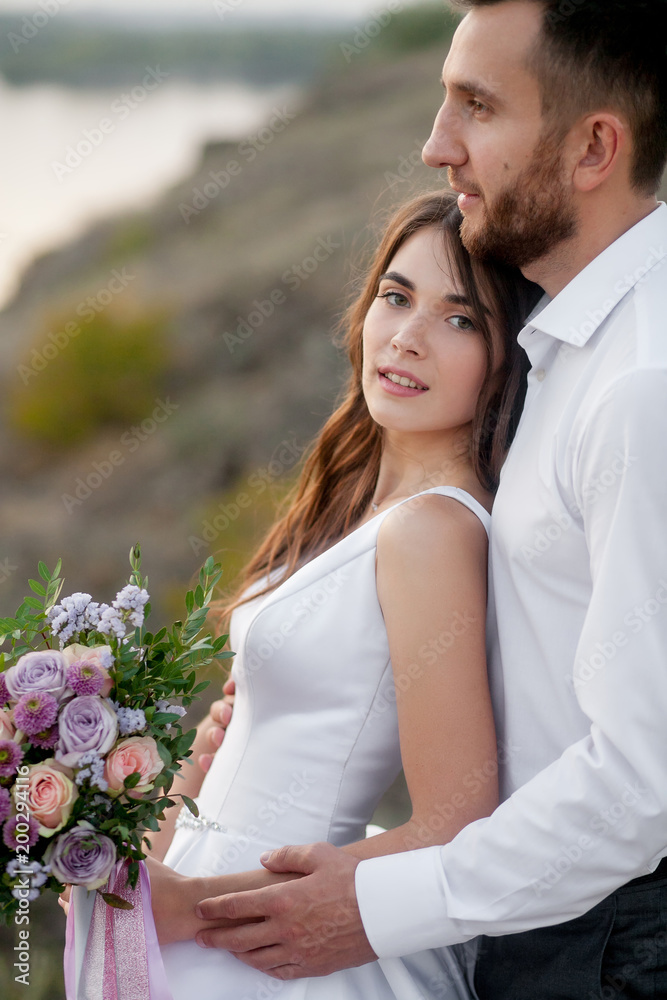 newly marriage beautiful couple, bride and groom, standing with wedding bouquet near river and mountains. Close-up newly marriage beautiful couple, bride and groom, standing with wedding bouquet near river and mountains. Close-up